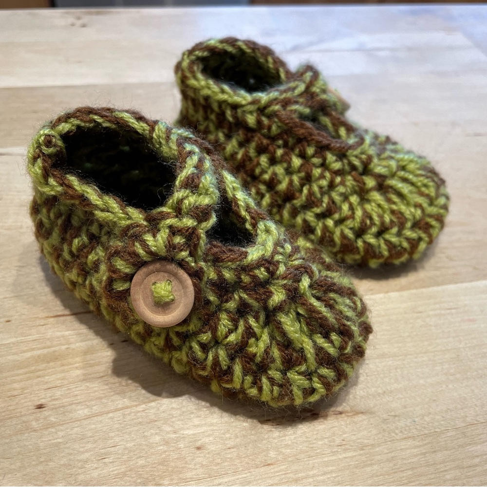 Knitted baby booties with straps and wooden buttons in green and brown